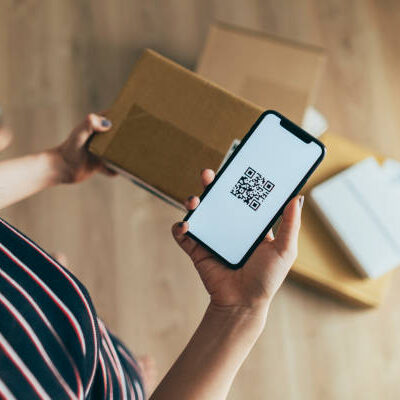 young Asian woman checking smartphone while receiving a parcel at home